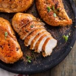 Golden-brown chicken breasts, sliced and served on a rustic plate with fresh herbs for garnish.